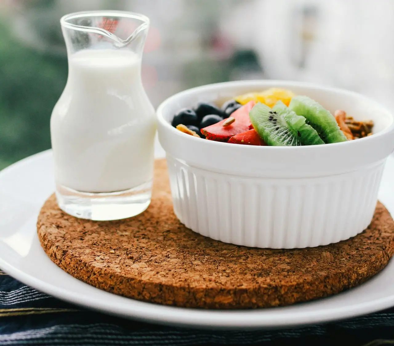 fruit salad inside bowl beside glass of milk on brown board